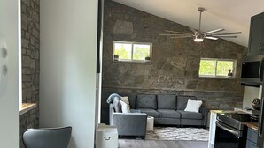 A modern kitchen with a stone accent wall, a grey sofa, and a ceiling fan.