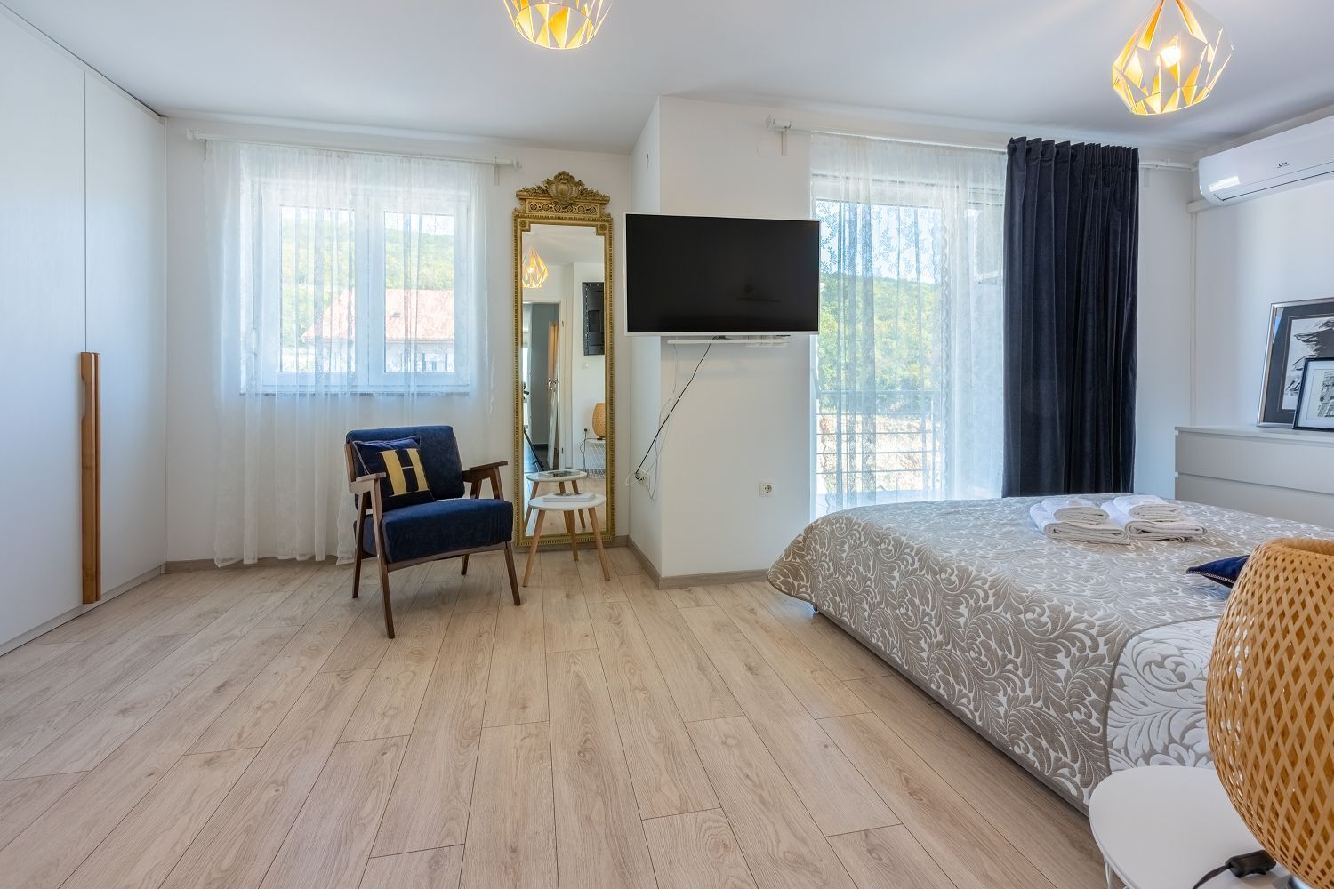 Et hotelværelse med seng, stol, spejl, fjernsyn og et vindue med gardiner.
