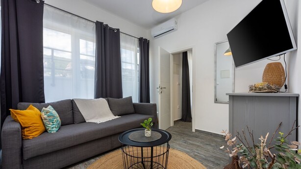 A modern living room with a grey sofa, a round black coffee table, and a small potted plant. There is a flat-screen TV mounted on the wall and a wicker basket on a shelf. - Modern flat with WiFi, air conditioning, 850 metre beach (Crikvenica)