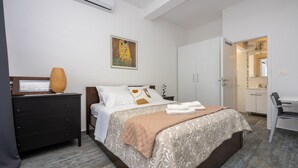 A bedroom with a bed, a dresser, a painting, and a bathroom visible through an open door. - Modern flat with WiFi, air conditioning, 850 metre beach (Crikvenica)
