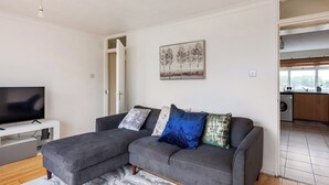 Un salon avec un canapé d’angle gris, un téléviseur à écran plat et un tableau accroché au mur.