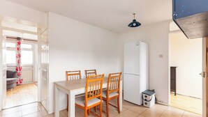 Une cuisine compacte comprenant une table à manger, quatre chaises, un réfrigérateur blanc et une petite poubelle.