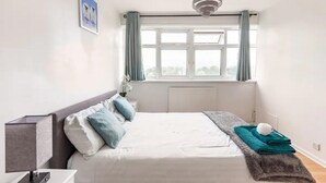 Une chambre à coucher comprenant un lit, une table de chevet, une lampe, une fenêtre avec des rideaux et un radiateur.