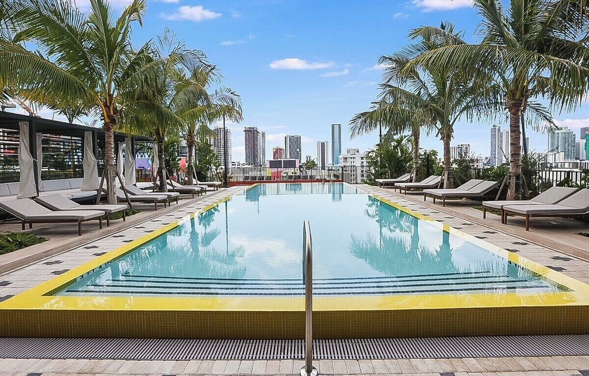 A swimming pool with lounge chairs, palm trees, and a city skyline in the background.