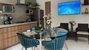 Una cocina moderna con comedor, que incluye una mesa de vidrio, sillas y un televisor montado en la pared.