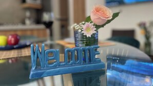 Un letrero azul que dice 'Welcome' sobre una mesa de vidrio, con una rosa y un pequeño jarrón de flores.