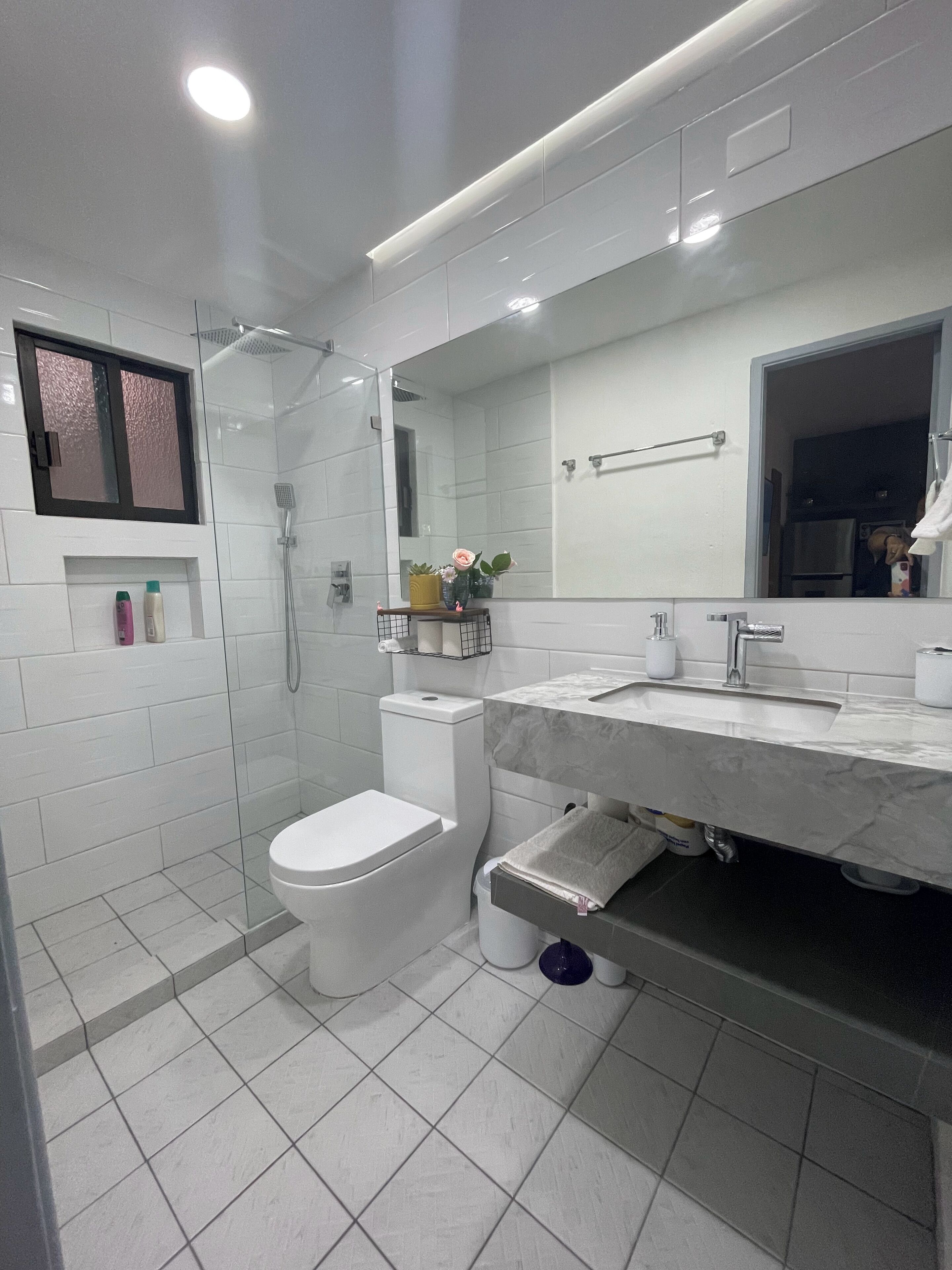 A modern bathroom with a glass-enclosed shower, a toilet, a sink with a marble countertop, and a mirror above the sink.