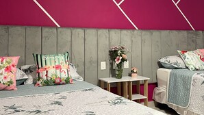 Un dormitorio con cabecera gris, ropa de cama floral y una pared de acento rosa.