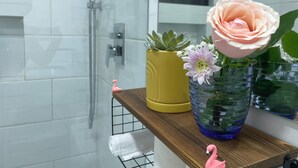 Un baño con cabina de ducha de vidrio, un estante de madera con un florero y un perchero para toallas.