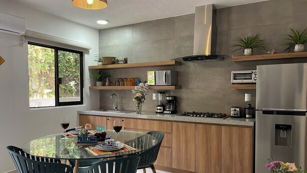 Una cocina moderna con una mesa de comedor de vidrio, armarios de madera y electrodomésticos de acero inoxidable.