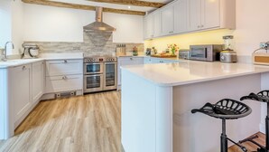 Una cocina moderna con gabinetes blancos, electrodomésticos de acero inoxidable, una isla central y vigas de madera a la vista.