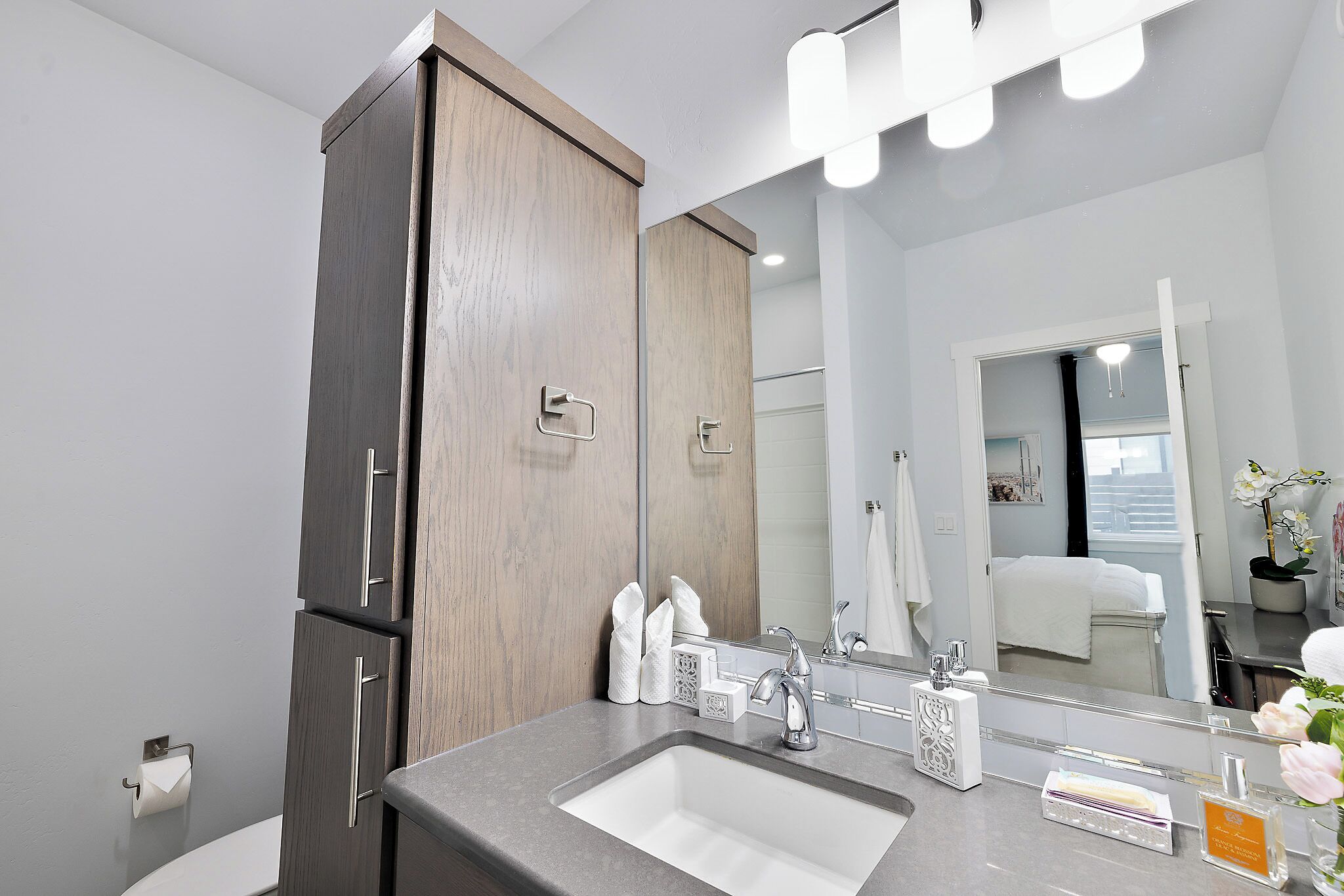 A modern bathroom with a grey sink, a large mirror, and a wooden cabinet.