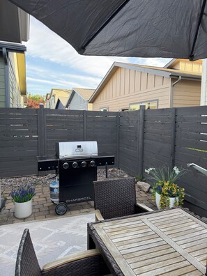 Un patio trasero con una parrilla, mobiliario exterior y una zona de terraza.
