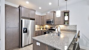 A modern kitchen with granite countertops, stainless steel appliances, and wooden cabinets. - Luxury Gated Coeur d’Alene Home Near Golf, Riverstone & Downtown. (Coeur d'Alene)