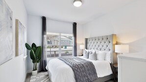 A modern hotel room with a large bed, a potted plant, a window with a view, and a bedside table with a lamp. - Luxury Gated Coeur d’Alene Home Near Golf, Riverstone & Downtown. (Coeur d'Alene)