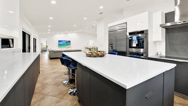 A modern kitchen with a large island, dark cabinetry, stainless steel appliances, and a seating area with bar stools. - Naples Oasis: Heated Pool, Gazebo, Grill Retreat (Naples)