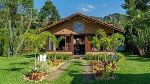Una casa de fusta rústica amb teulada d'estries, envoltada de vegetació exuberant i un jardí ben cuidat.