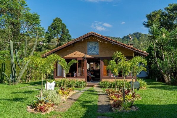 Una casa de madera rústica con techo de tejas, rodeada de abundante vegetación y un jardín cuidado.