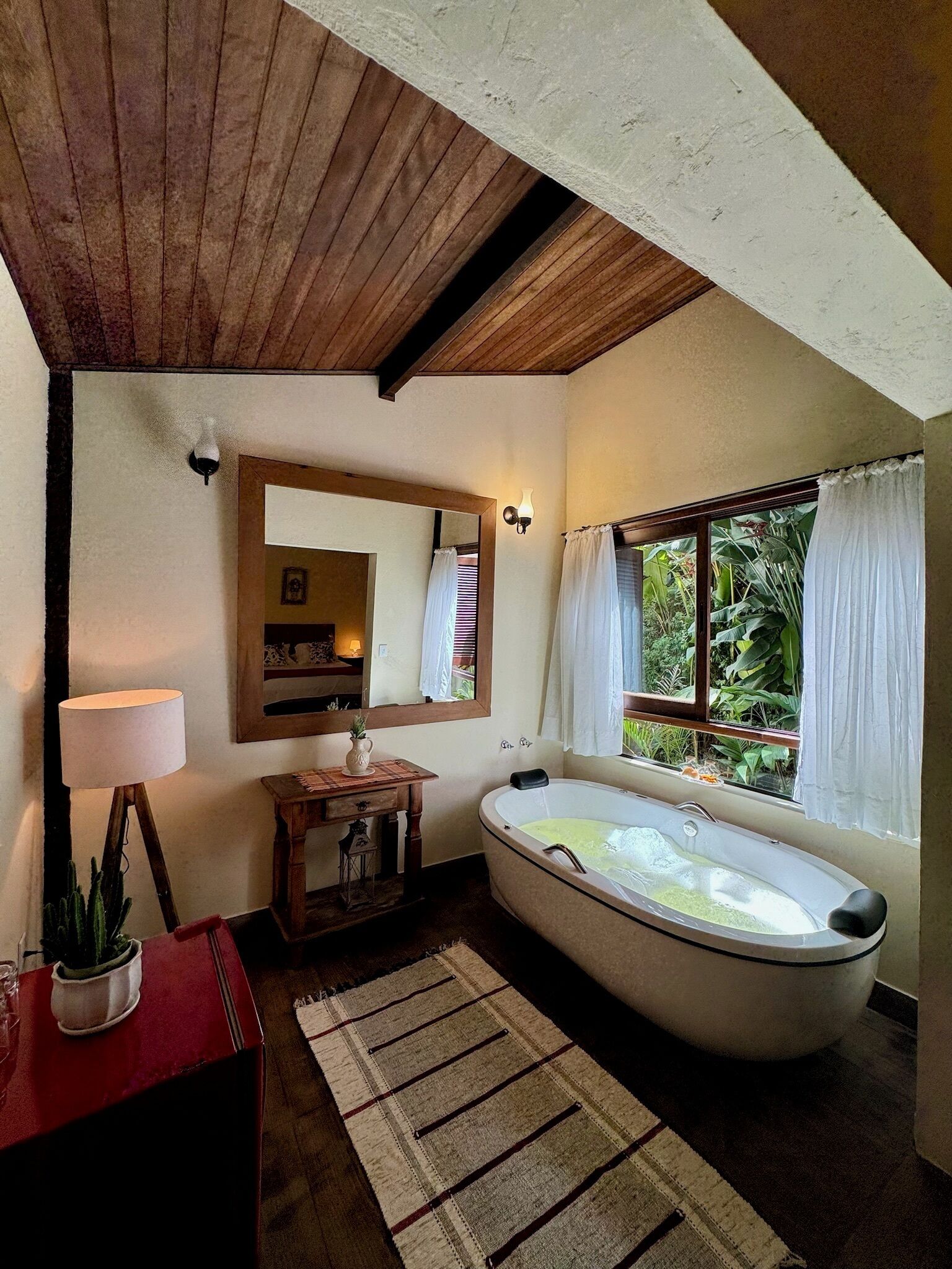 Un baño con una bañera independiente, un tocador de madera, un espejo y una ventana con cortinas.