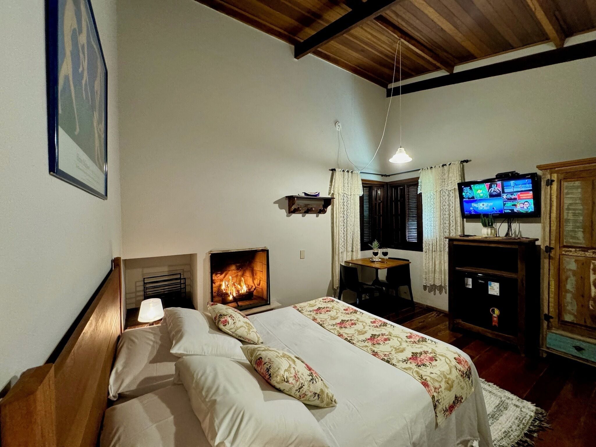 A cozy room with a bed, a fireplace, a television, and a wooden ceiling.