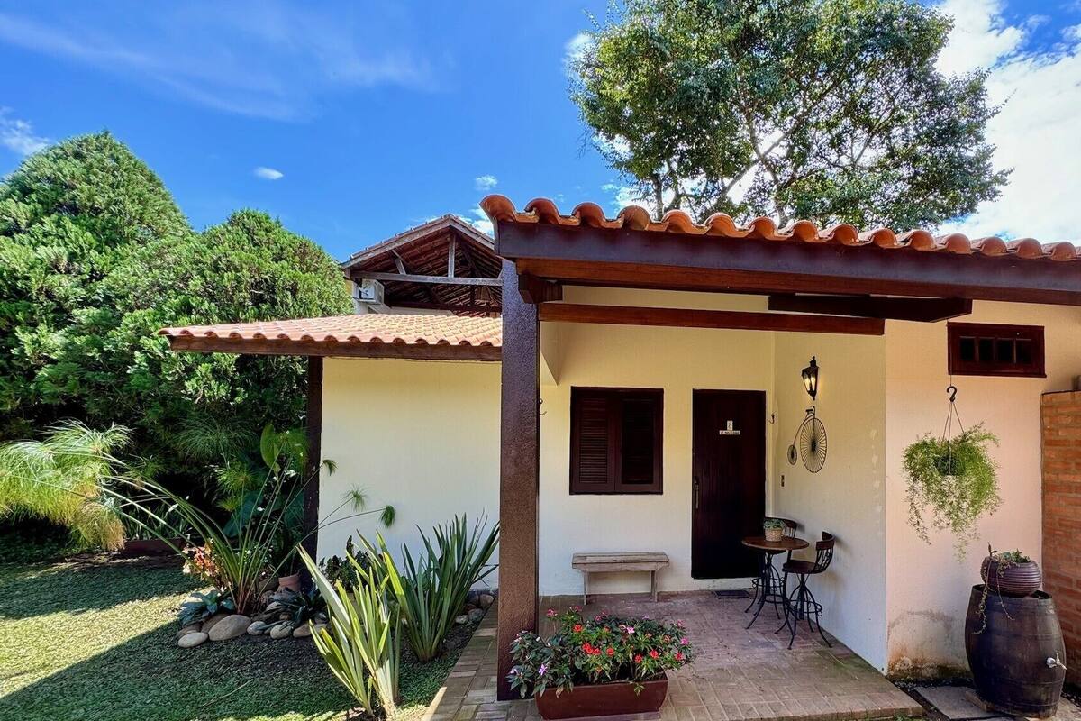 Una pequeña casa de un piso con techo de tejas, un patio con mesa y sillas, y un jardín con diversas plantas.