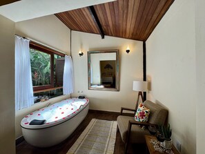 Un baño con una bañera independiente, una ventana con cortinas, un espejo, una lámpara y una silla.