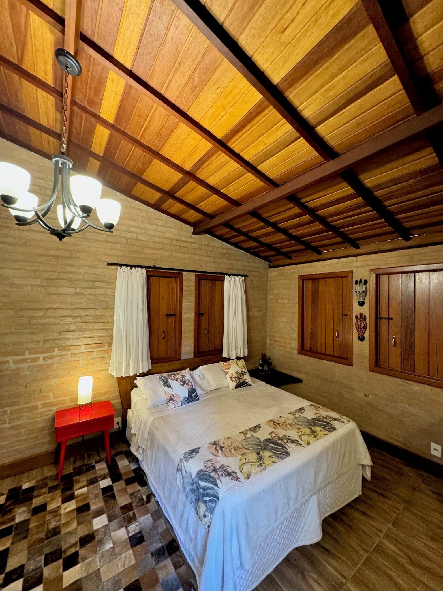 Un dormitorio con piso a cuadros, cama con ropa de cama floral, vigas de madera en el techo y un candelabro.