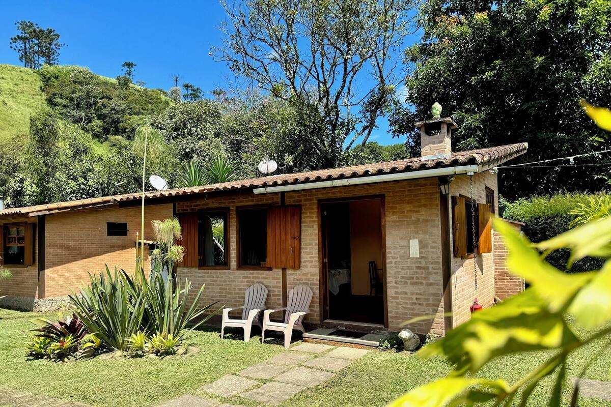 Una pequeña casa de ladrillo con techo de tejas, una puerta principal y un porche pequeño con dos sillas.