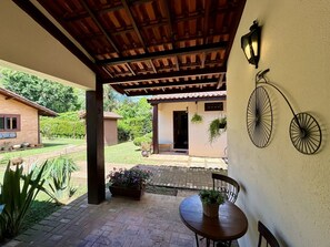 Un patio cubierto con una mesa, sillas, una planta colgante y un aplique de pared.
