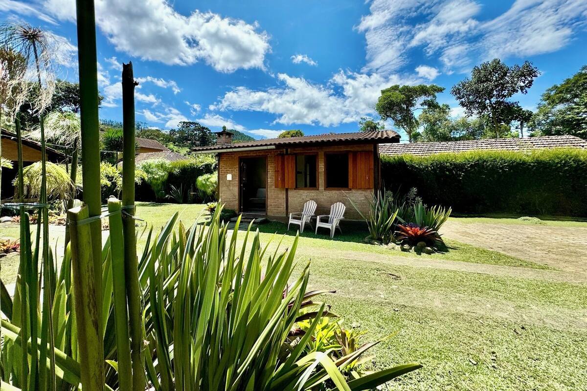 Una casa pequeña con techo de tejas, rodeada de un césped cuidado y diversas plantas.
