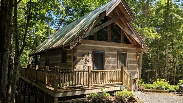 A rustic cabin with a wooden deck and a metal roof, surrounded by trees.