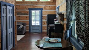 A rustic cabin interior with a wooden dining table, a sofa, and a kitchen area.