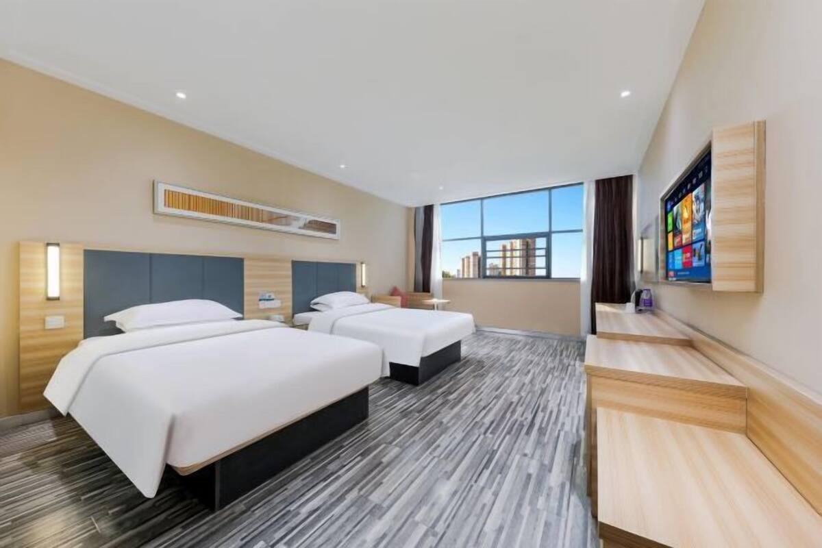 Ein Hotelzimmer mit zwei Betten, einem Fernseher, einem Schreibtisch und einem großen Fenster.