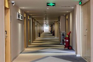 A hotel corridor with doors on both sides, a fire extinguisher, and a sign indicating the direction to the exit. - Jinxuan Hotel (Zhengzhou South Third Ring Road) (Zhengzhou)