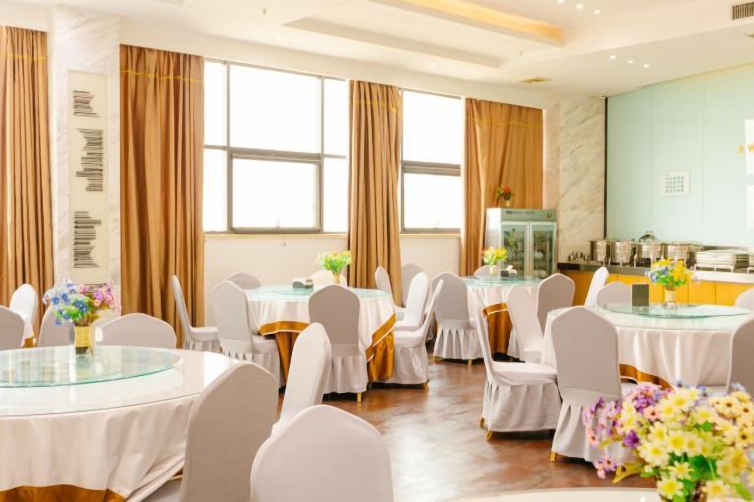 Uma sala de banquetes com mesas redondas, cadeiras brancas e arranjos florais.