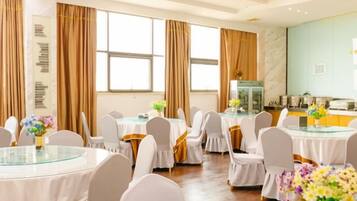 Uma sala de banquetes com mesas redondas, cadeiras brancas e arranjos florais.