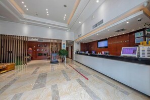 Een hotel receptie met een receptiebalie, een televisiescherm en een plant.