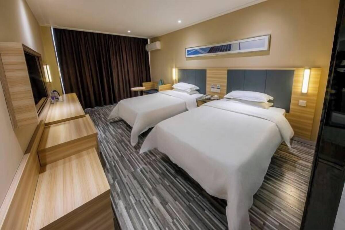 Ein Hotelzimmer mit zwei Betten, einem Schreibtisch, einem Sessel, einem Fernseher und einem großen Fenster mit Vorhängen.