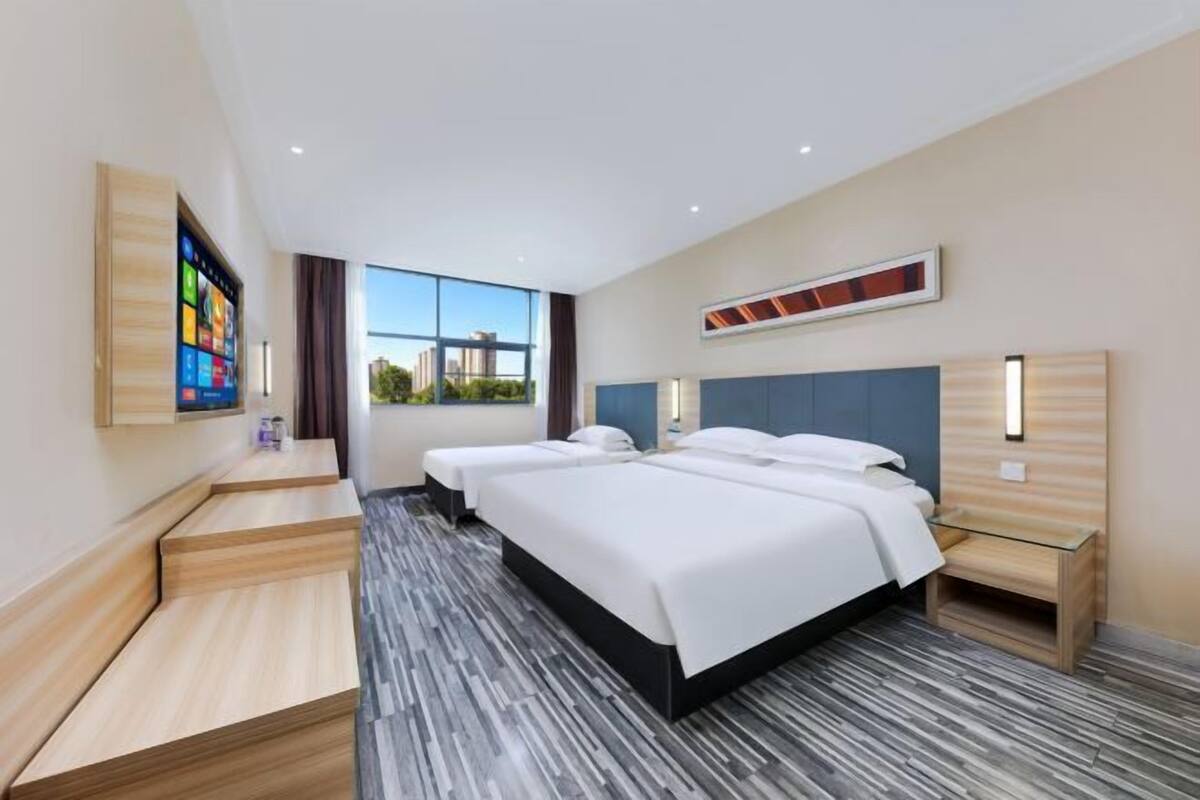 Ein Hotelzimmer mit zwei Betten, einem großen Fenster, einem Fernseher und einer hölzernen Bank.