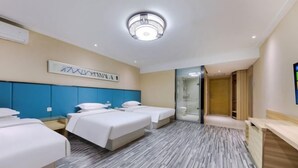 Ein Hotelzimmer mit zwei Betten, einem Schreibtisch, einem Spiegel und einem durch eine Glastür einsehbaren Badezimmer.