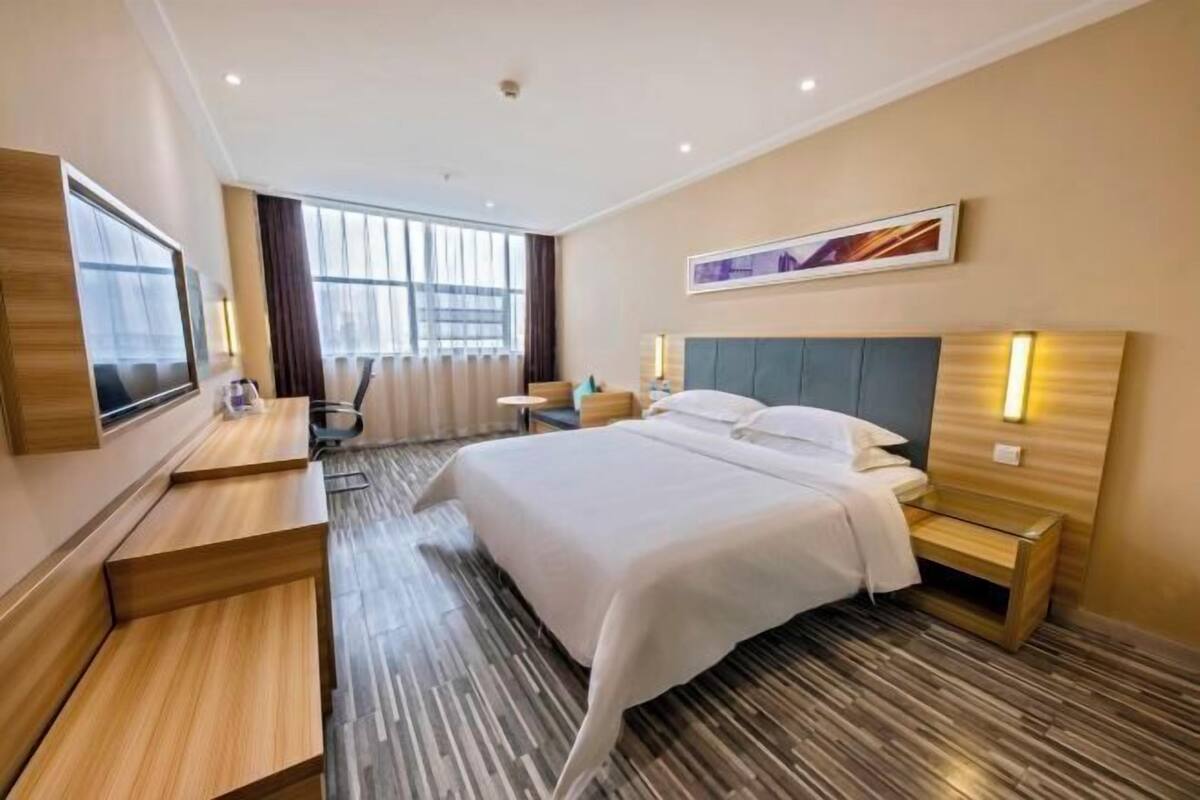 Ein Hotelzimmer mit einem großen Bett, einem Schreibtisch, einem Sessel, einem Fernseher und einem Fenster mit Vorhängen.
