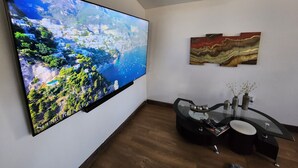 Un salon moderne doté d’un grand téléviseur à écran plat fixé au mur, d’une table basse en verre et d’un style de décoration minimaliste.