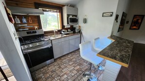 Une cuisine compacte équipée d’une cuisinière, d’un four et d’un évier. On y trouve des tabourets de bar blancs et un petit comptoir de bar.