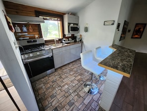 A compact kitchen with a stove, oven, and sink. There are white bar stools and a small bar counter.