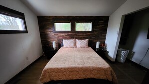Une chambre avec un grand lit, deux fenêtres, un mur en bois et une poubelle.