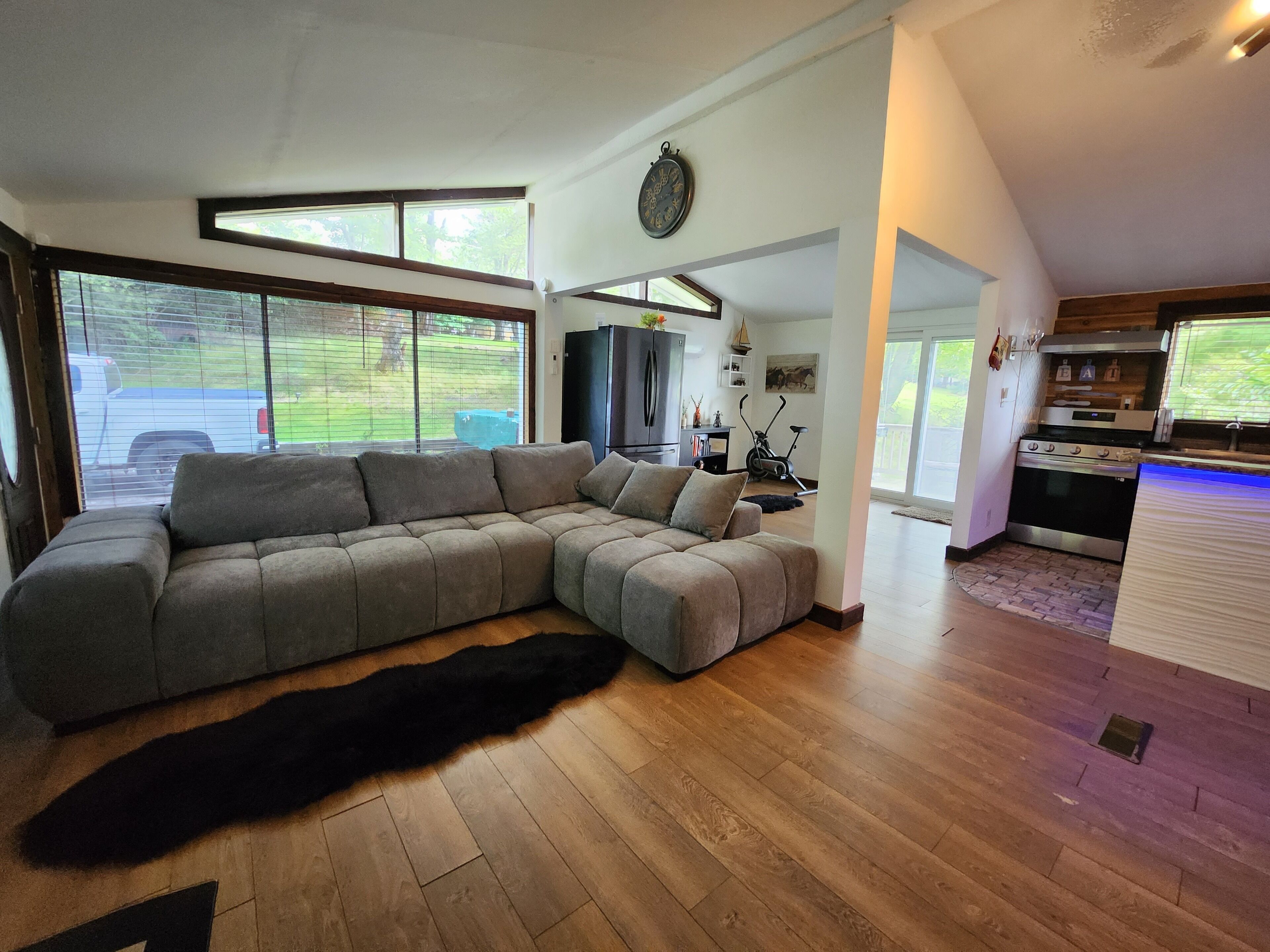 Una sala de estar moderna con un sofá seccional, un ventanal grande y una zona de cocina.