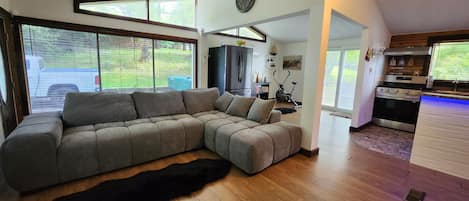 Una sala de estar moderna con un sofá seccional, un ventanal grande y una zona de cocina.