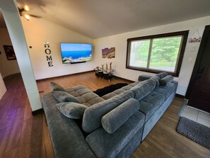 Una sala de estar moderna con un sofá gris, un televisor de pantalla plana y una ventana con persianas.