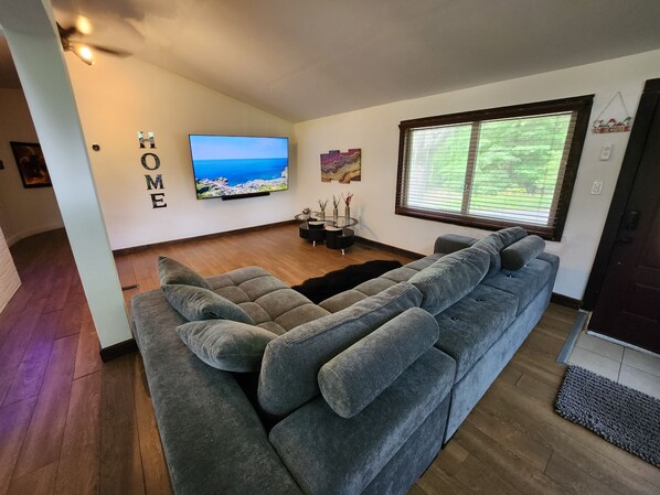 Una sala de estar moderna con un sofá gris, un televisor de pantalla plana y una ventana con persianas.