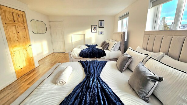 A bedroom with two beds, a wooden door, a window with a view, and a ceiling light. - Spacious Haven with Free Parking (Glasgow)